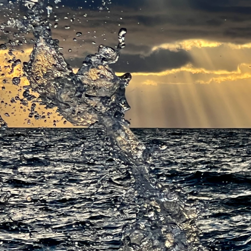 Waves splash dramatically in the foreground of a dark ocean, with golden sunlight streaming through clouds in the background—an inspiring scene that captures both the power and beauty sought after in e-commerce imagery.