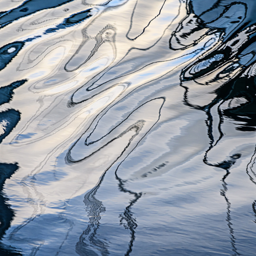Abstract ripples and reflections on water, featuring wavy lines and patterns in shades of blue, white, and gray, creating a dynamic, fluid appearance.