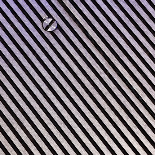 Diagonal metal slats with a single screw head visible near the top left, creating a repeating pattern across the surface—an aesthetic detail often sought after in e-commerce product photography. The lighting gives the metal a slight purple hue.